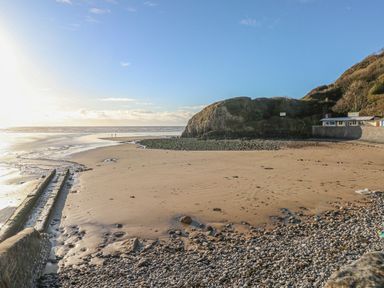 A beach with a rocky shoreline and a small building near cliffs at Little Brook Cottage in Laugharne