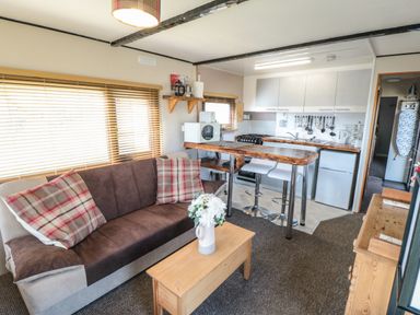 A small living area with a sofa and kitchen with bar stools and a wooden coffee table at Castle View Cabin in Cloughton