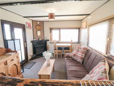 A living room with a brown sofa, wooden coffee table, dining table with chairs, fireplace, and wooden cabinet at Castle View Cabin in Cloughton