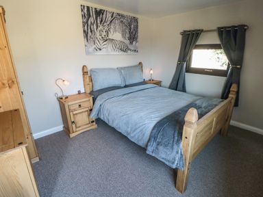 A bedroom with a wooden bed and nightstands with lamps a window with curtains and a tiger picture on the wall at Castle View Cabin in Cloughton