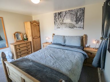 A bedroom with a wooden bed a dresser wardrobe bedside tables and a tiger painting at Castle View Cabin in Cloughton
