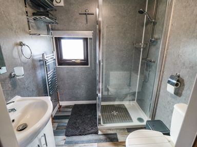 A bathroom with a shower enclosure, toilet, sink, towel rack, window, and floor mat at Castle View Cabin in Cloughton