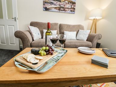 A living room with a brown sofa pillows a floor lamp and a wooden coffee table with wine grapes crackers and a cutting board at Station View in Whitby