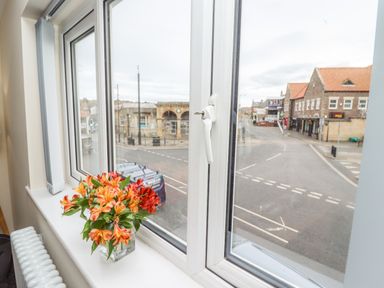 A window with flowers on the windowsill overlooking a street with buildings and vehicles at Station View in Whitby