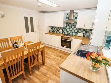 A kitchen with wooden dining table and chairs white cabinets tiled backsplash and flowers on the counter at Station View in Whitby