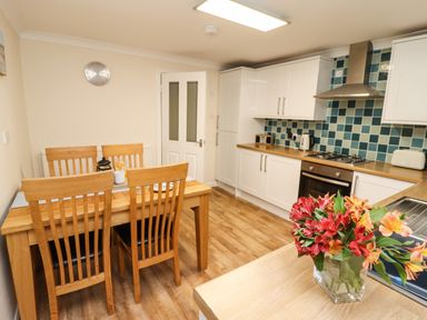 A kitchen and dining area with wooden table and chairs flowers on the counter and tiled backsplash at Station View in Whitby