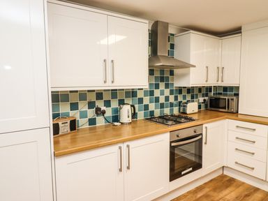 A kitchen with white cabinets a wooden countertop a stove oven kettle toaster microwave and a radio at Station View in Whitby