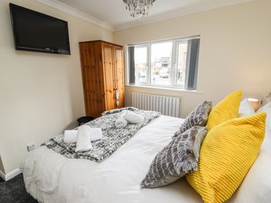 A bedroom with a bed with yellow and gray pillows a wooden wardrobe a wall-mounted tv and a window showing a street view at Station View in Whitby