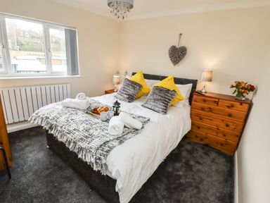 A bedroom with a double bed with pillows and blankets bedside tables with lamps a wooden chest of drawers and a window at Station View in Whitby