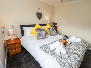 A bedroom with a double bed with yellow and gray pillows bedside tables with lamps and a tray with croissants and cups on the bed at Station View in Whitby