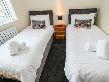 A bedroom with two single beds white bedding decorative pillows nightstand with lamp and rolled towels at Station View in Whitby