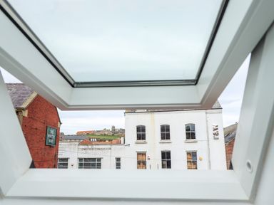 View of buildings and a hill with ruins through an open skylight window at Station View in Whitby
