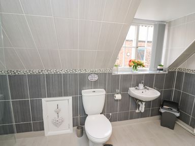 A bathroom with a toilet and sink under a slanted ceiling with a window and flowers on the windowsill at Station View in Whitby
