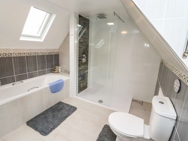 A bathroom with a bathtub a shower area a toilet and two rugs at Station View in Whitby