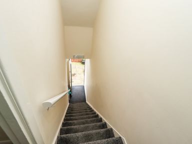 A narrow staircase with dark carpet and a white handrail leading to an open door at Station View in Whitby