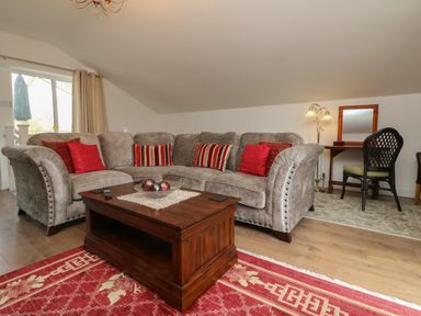 A living room with a grey sectional sofa with red and striped cushions a wooden coffee table and a desk with a chair at Scenic Views in High Bickington