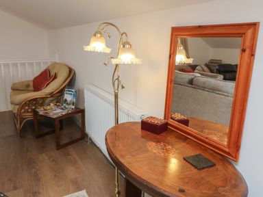 A corner with a cushioned wicker chair next to a small table with magazines a wooden table with a framed mirror and a floor lamp at Scenic Views in High Bickington