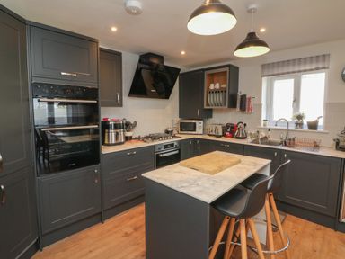 A kitchen with dark cabinets a kitchen island with stools and appliances at Scenic Views in High Bickington