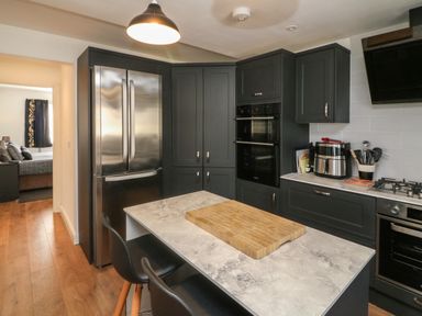A kitchen with dark cabinets a stainless steel refrigerator double ovens a gas stove an island with a wooden cutting board and two black chairs at Scenic Views in High Bickington