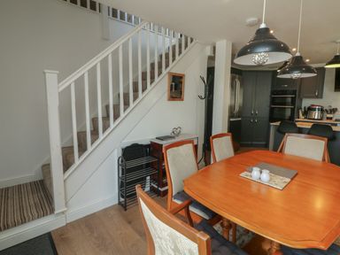 A dining area with a wooden table and chairs next to stairs and a kitchen with black cabinets and stainless steel refrigerator at Scenic Views in High Bickington