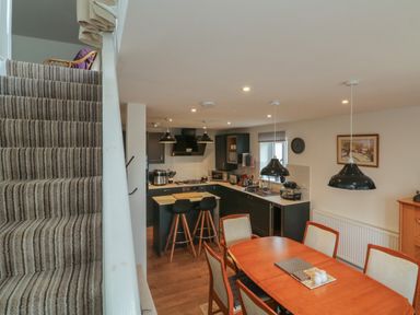 A kitchen and dining area with wooden table chairs island with stools and carpeted stairs at Scenic Views in High Bickington