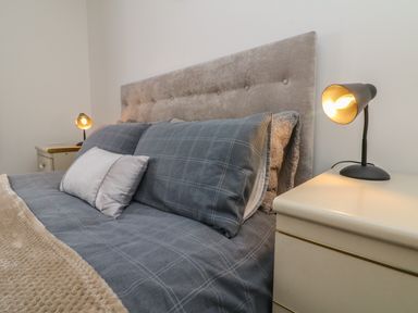 A bed with a padded headboard grey checked bedding a beige blanket two bedside tables with lamps at Scenic Views in High Bickington