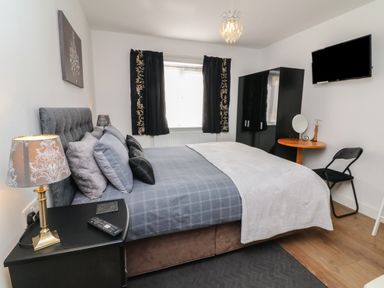 A bedroom with a double bed a bedside table a wardrobe a wall-mounted tv and a small round table with a chair at Scenic Views in High Bickington