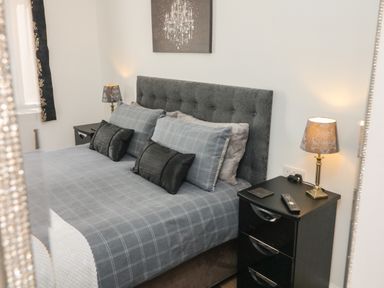 A bedroom with a bed with gray headboard and checked bedding bedside tables with lamps and a framed picture above the bed at Scenic Views in High Bickington