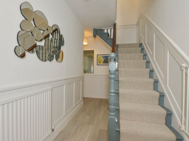 A hallway with a staircase carpet runner and circular mirrors on the wall at Beachcomber in Padstow