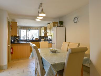 A kitchen and dining area with a table covered by a cloth and chairs at Beachcomber in Padstow