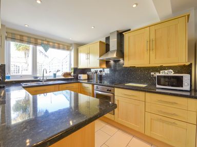 A kitchen with wooden cabinets black countertops a sink oven microwave and window at Beachcomber in Padstow