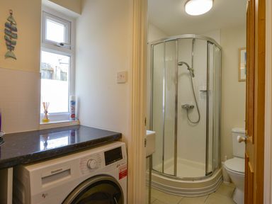A bathroom with a shower enclosure sink and toilet next to a laundry area with a washing machine and window at Beachcomber in Padstow