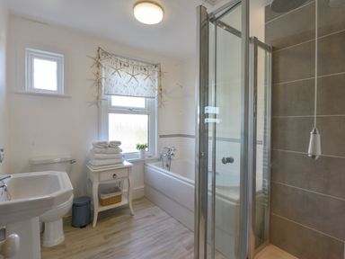 A bathroom with a bathtub a shower a sink a toilet and a small table with towels at Beachcomber in Padstow