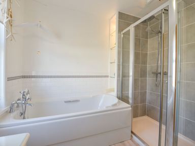 A bathroom with a white bathtub and a glass-enclosed shower with tiled walls at Beachcomber in Padstow