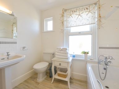 A bathroom with a toilet sink bathtub towels on a small table and a window with a seagull patterned blind at Beachcomber in Padstow
