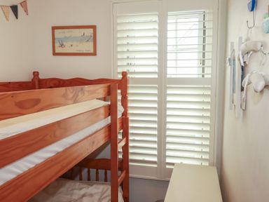 A bedroom with a bunk bed and window shutters at Beachcomber in Padstow