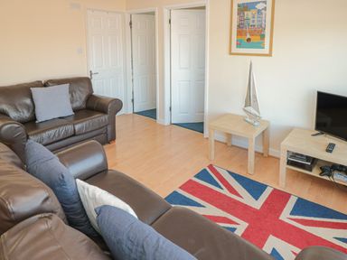 A living room with brown leather sofas pillows two white doors a television on a wooden stand a small wooden table with a model sailboat and a Union Jack rug at 304 Norton Park Dartmouth