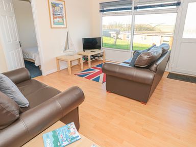 A living room with two brown sofas a television on a stand a small table with a model sailboat and a door leading to a bedroom at 304 Norton Park in Dartmouth