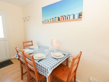 A dining area with a table covered by a blue and white checkered tablecloth set for four with wooden chairs and a framed picture of colorful beach huts on the wall at 304 Norton Park in Dartmouth