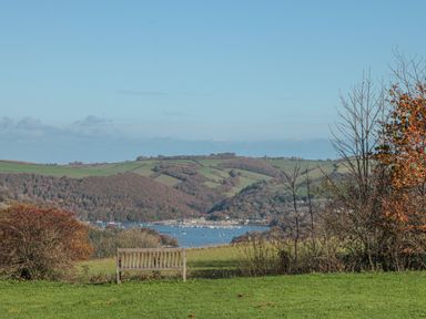 A wooden bench on a grassy hill overlooking a river with boats and hills in the background at 304 Norton Park in Dartmouth