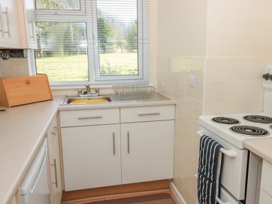 A kitchen with a sink under a window a dish rack a breadbox and an electric stove with oven mitts at 304 Norton Park in Dartmouth