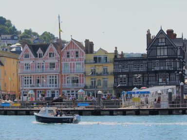 A small motorboat on the water near a pier with people walking and colorful buildings in the background at 304 Norton Park in Dartmouth