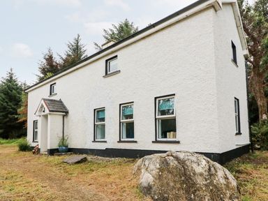 A white two-story house with multiple windows and a front porch surrounded by trees and grass at Kealduff Lower in Glenbeigh County Kerry