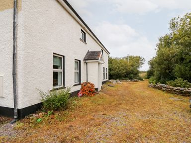 A white house with black trim next to a dirt driveway and trees at Kealduff Lower in Glenbeigh County Kerry