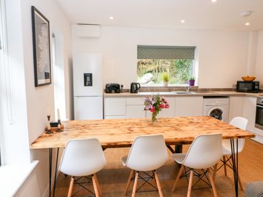A kitchen with wooden dining table and white chairs with flowers in a vase on the table at Kealduff Lower in Glenbeigh County Kerry