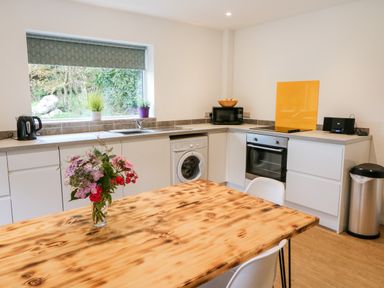 A kitchen with white cabinets a wooden dining table with flowers a washing machine an oven a microwave a kettle and a window with plants at Kealduff Lower Glenbeigh County Kerry