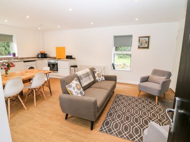 A living room with gray sofa and armchairs a dining table with white chairs and an open kitchen in the background at Kealduff Lower in Glenbeigh County Kerry