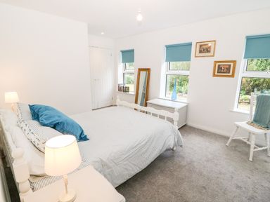 A bedroom with a bed a bedside table with a lamp a chair a chest and windows with blue blinds at Kealduff Lower in Glenbeigh County Kerry