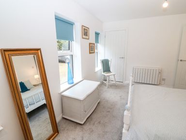 A bedroom with a bed a white chest two windows with blue blinds a wooden chair a full length mirror and framed pictures at Kealduff Lower Glenbeigh County Kerry