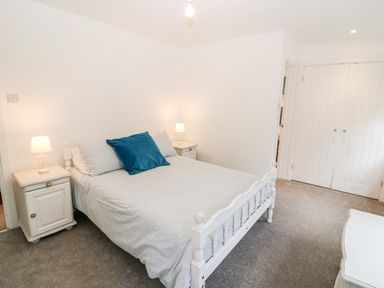 A bedroom with a bed with striped bedding and blue pillow two bedside tables with lamps and white wardrobe doors at Kealduff Lower in Glenbeigh County Kerry